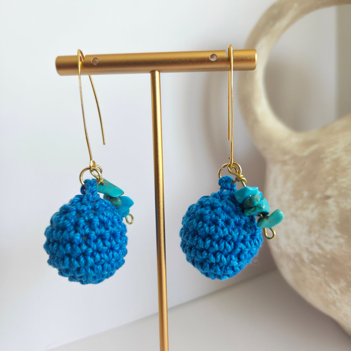 Blue crochet earrings with gemstone chips on a gold stand with a neutral background