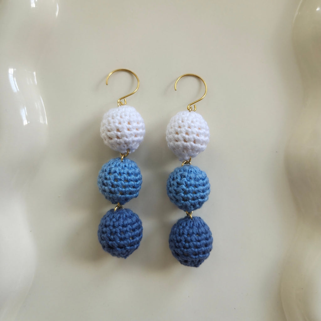 Blue crocheted ball earrings in white, blue, and gold on a beige background