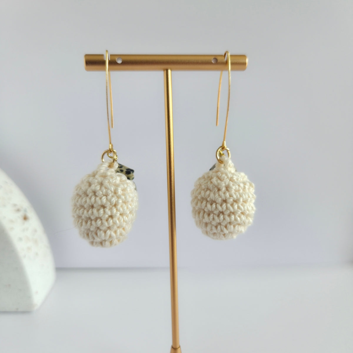Pair of cream crochet ball earrings on a gold earring stand against a light background