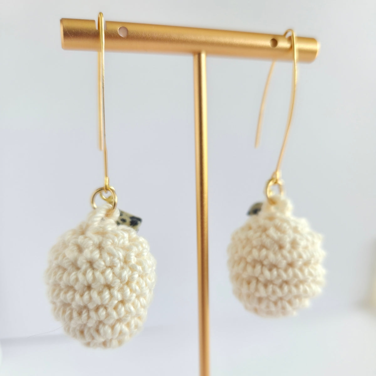 Pair of cream crochet earrings on a gold earring stand against a white background