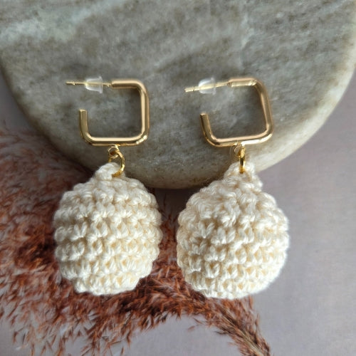 Pair of gold hoop crochet earrings with cream crocheted balls on a stone surface.