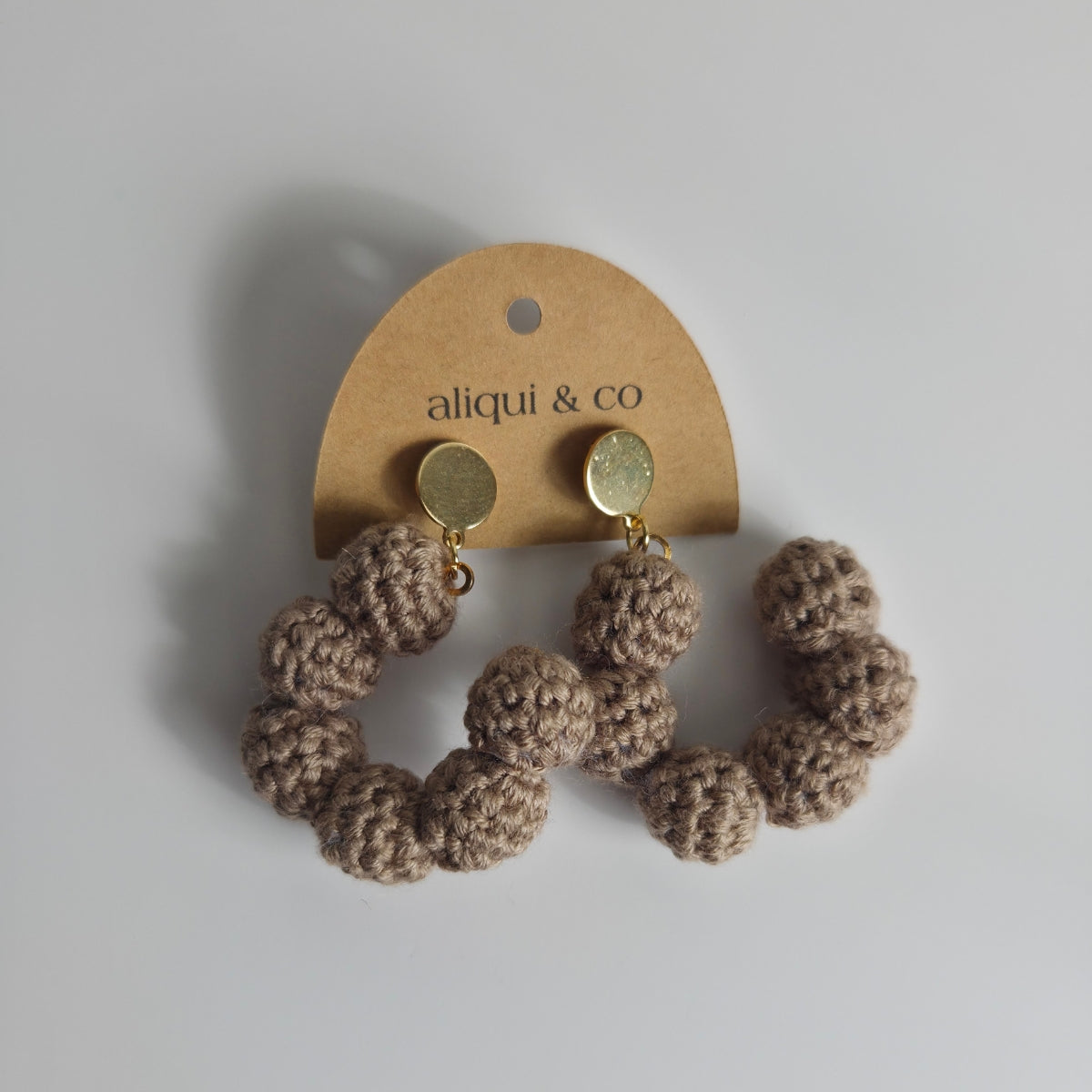 Crocheted ball earrings on a 'aliqui & co' branded card against a light background