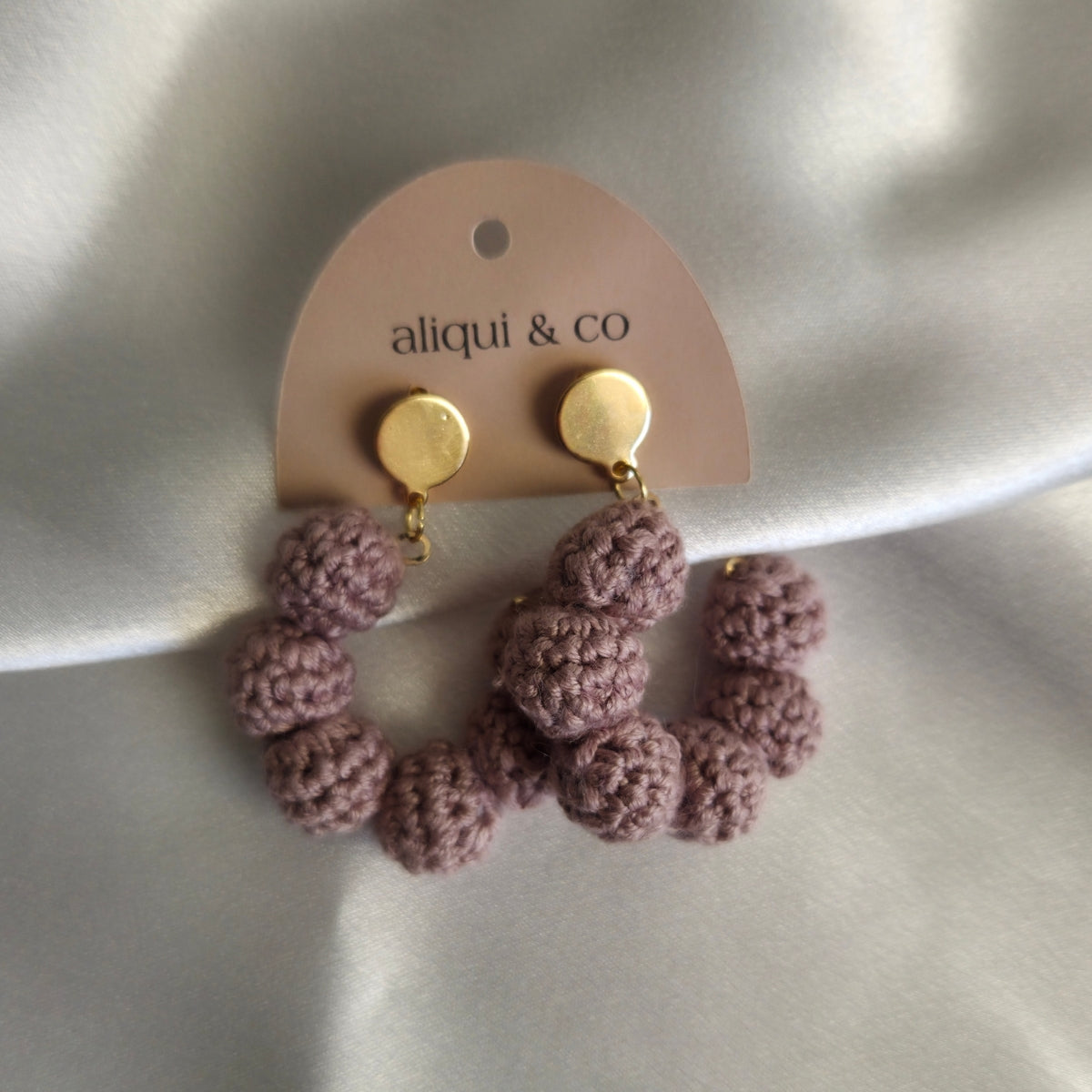 Pair of earrings with gold posts on a 'aliqui & co' branded card against a neutral background