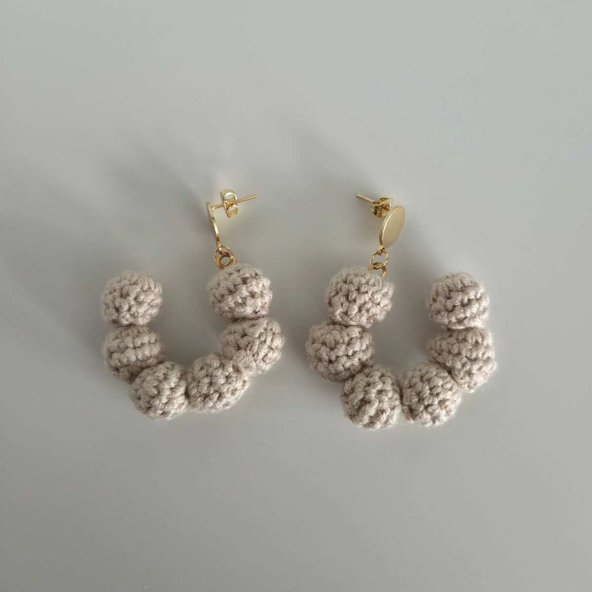 Pair of beige crocheted hoop earrings on a light gray background
