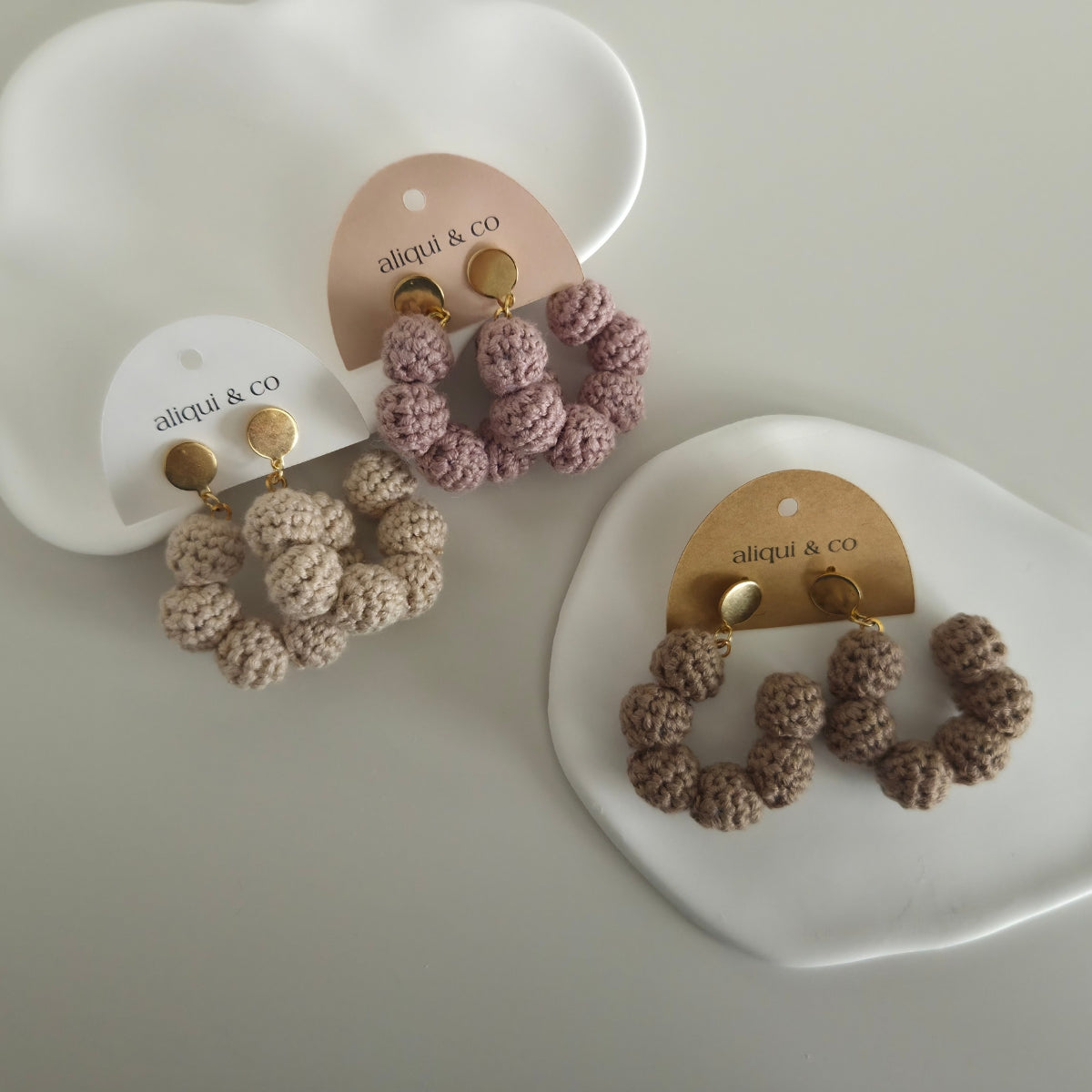 Pair of knitted earrings on 'aliqui & co' branded cards against a white background