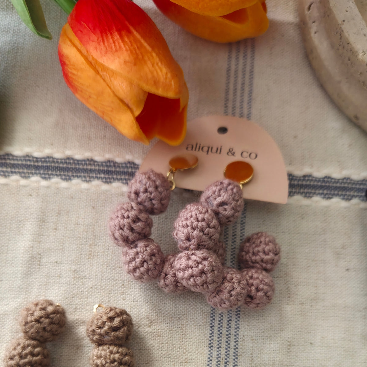 Crocheted earrings on a textured surface with a tulip in the background