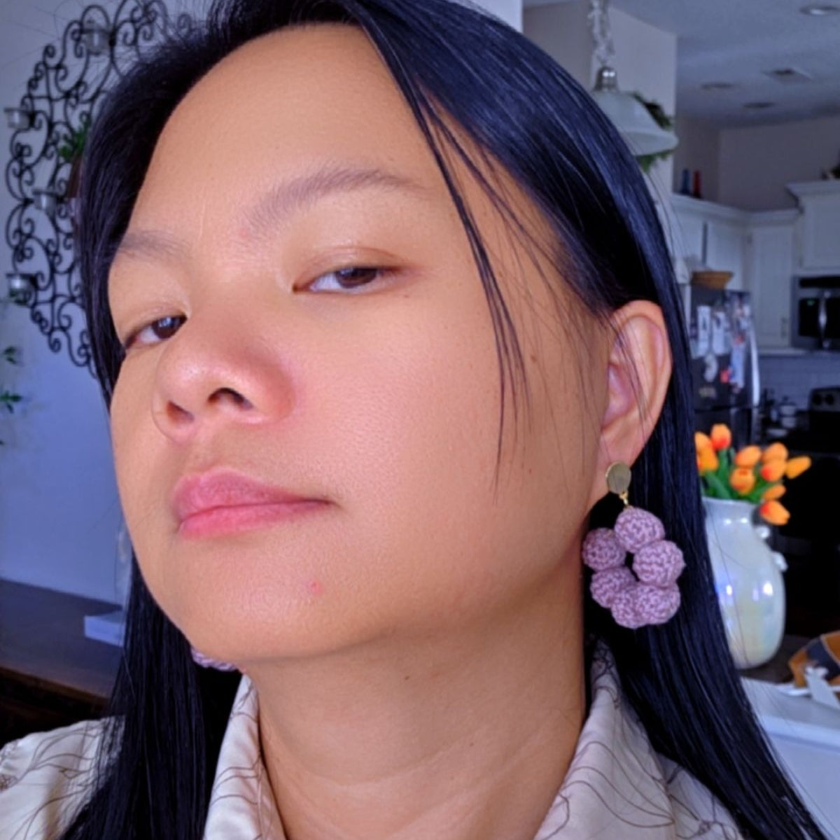 Close-up of a person wearing pink crescent crochet earrings in a kitchen setting