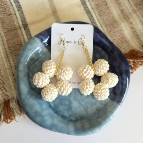 Pair of cream ball earrings on a blue dish with a branded card
