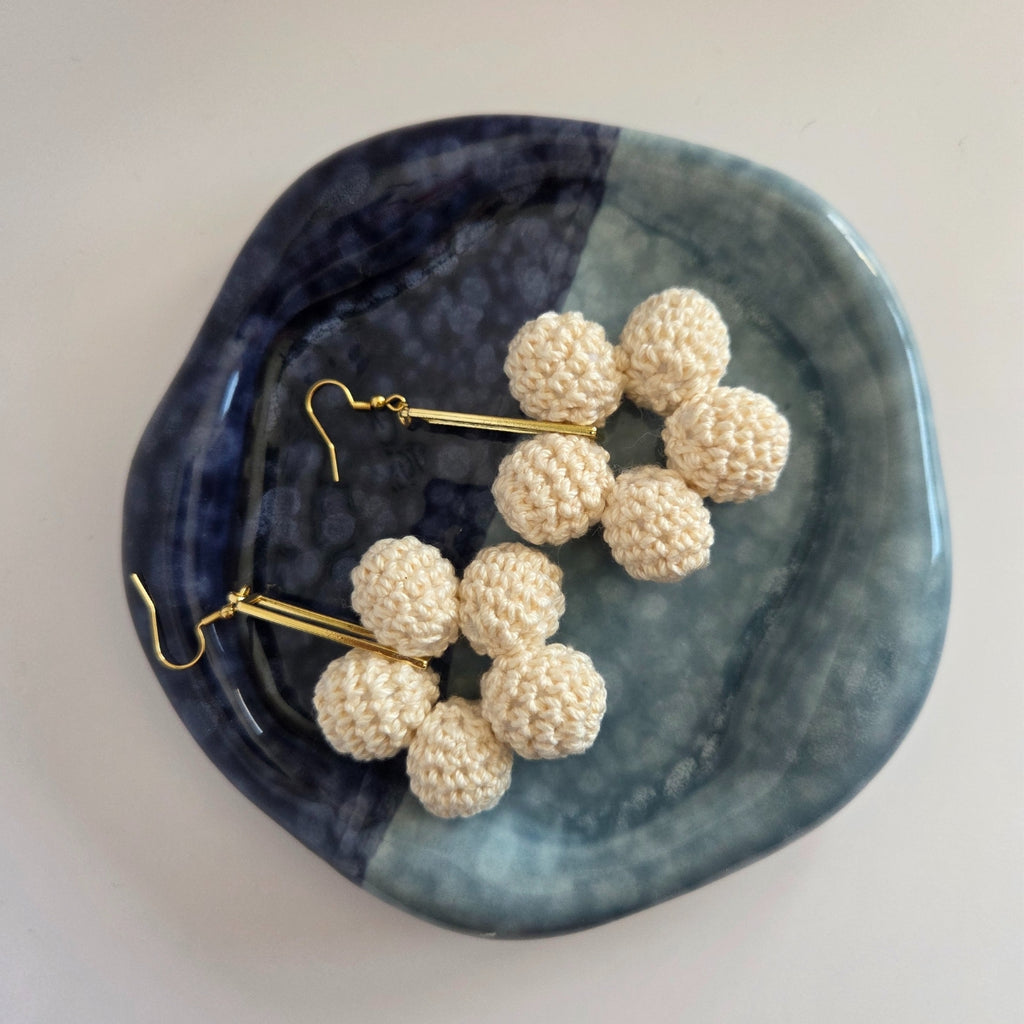 Pair of beige spherical earrings on a blue and black ceramic dish.
