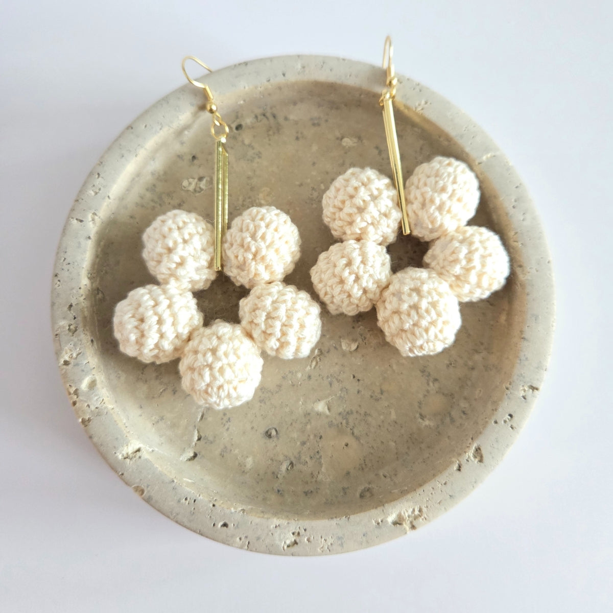White spherical earrings on a concrete dish with a white background