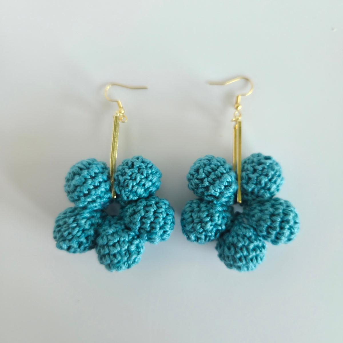 Pair of warm teal flower-shaped earrings on gold hooks against a white background