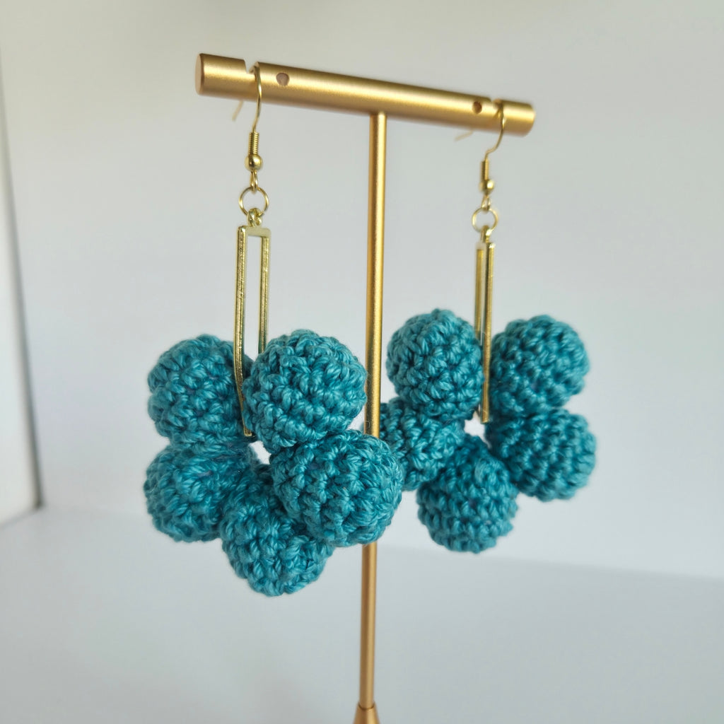 Teal crocheted earrings on a gold earring stand against a white background