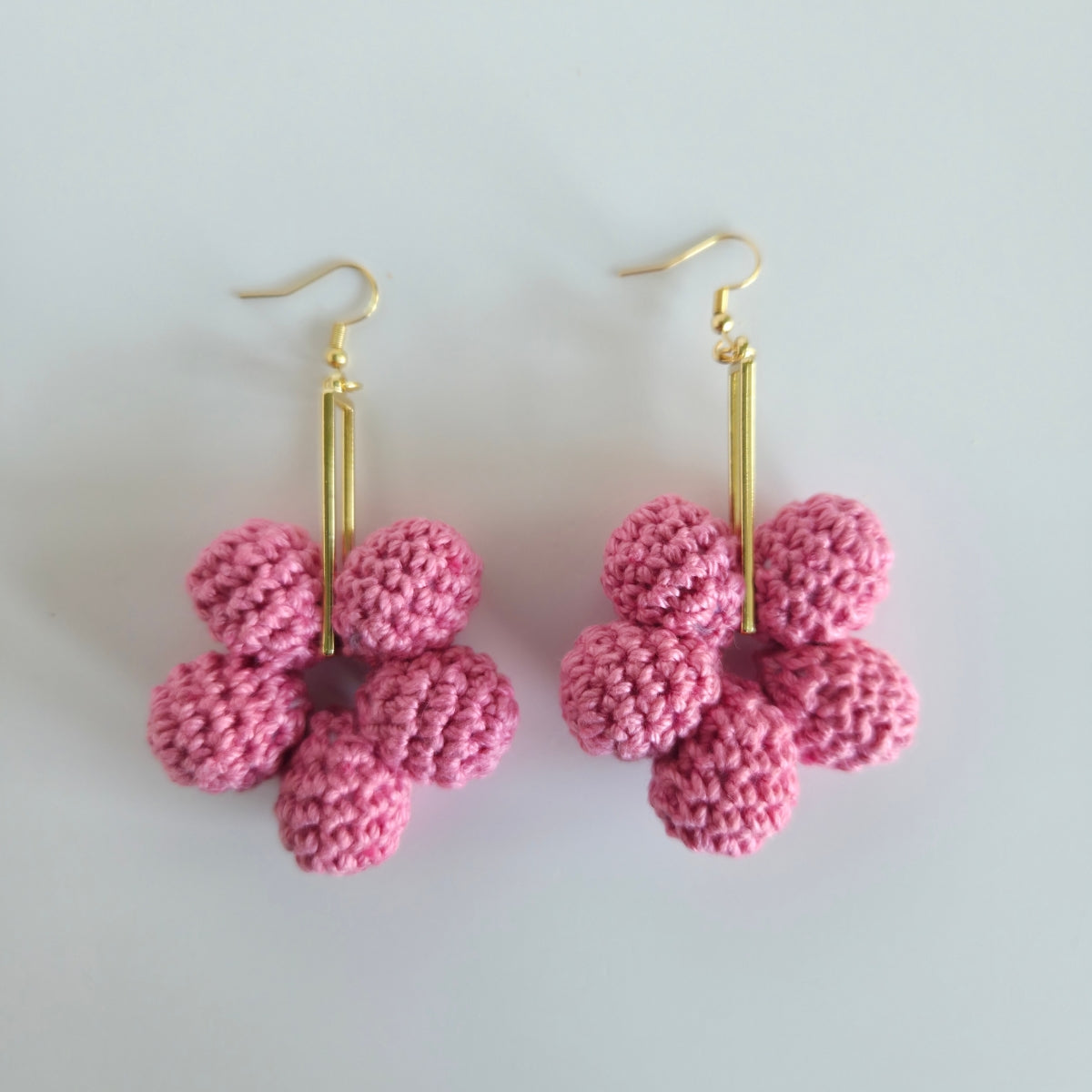 Warm rose pink crocheted flower earrings with gold hooks on a light gray background