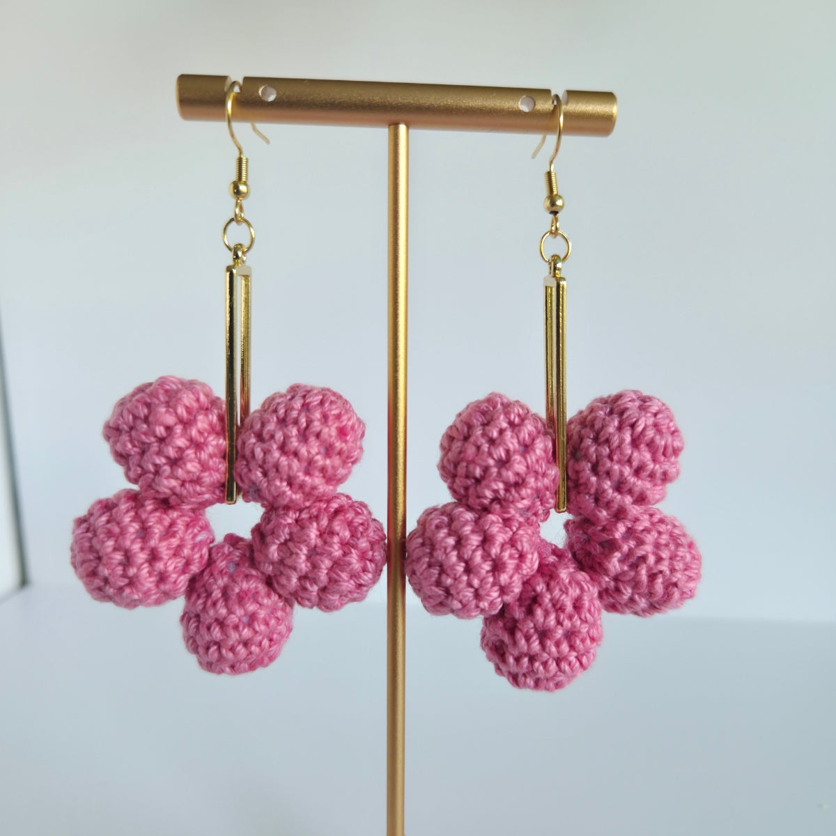 Pink crocheted ball earrings on a gold stand against a white background