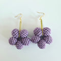 Purple flower-shaped earrings on gold hooks against a light background