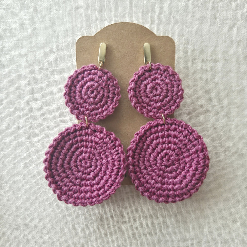 Dusty rose crochet earrings on a beige card against a light fabric background
