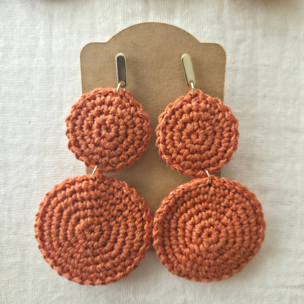 Pair of ginger orange crochet earrings on a beige card against a light background