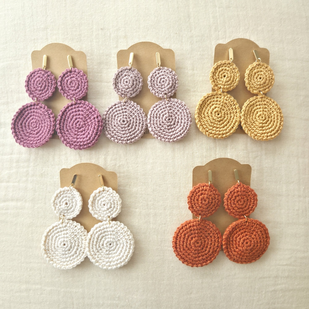 Set of four pairs of boho round earrings in different colors on beige display cards.