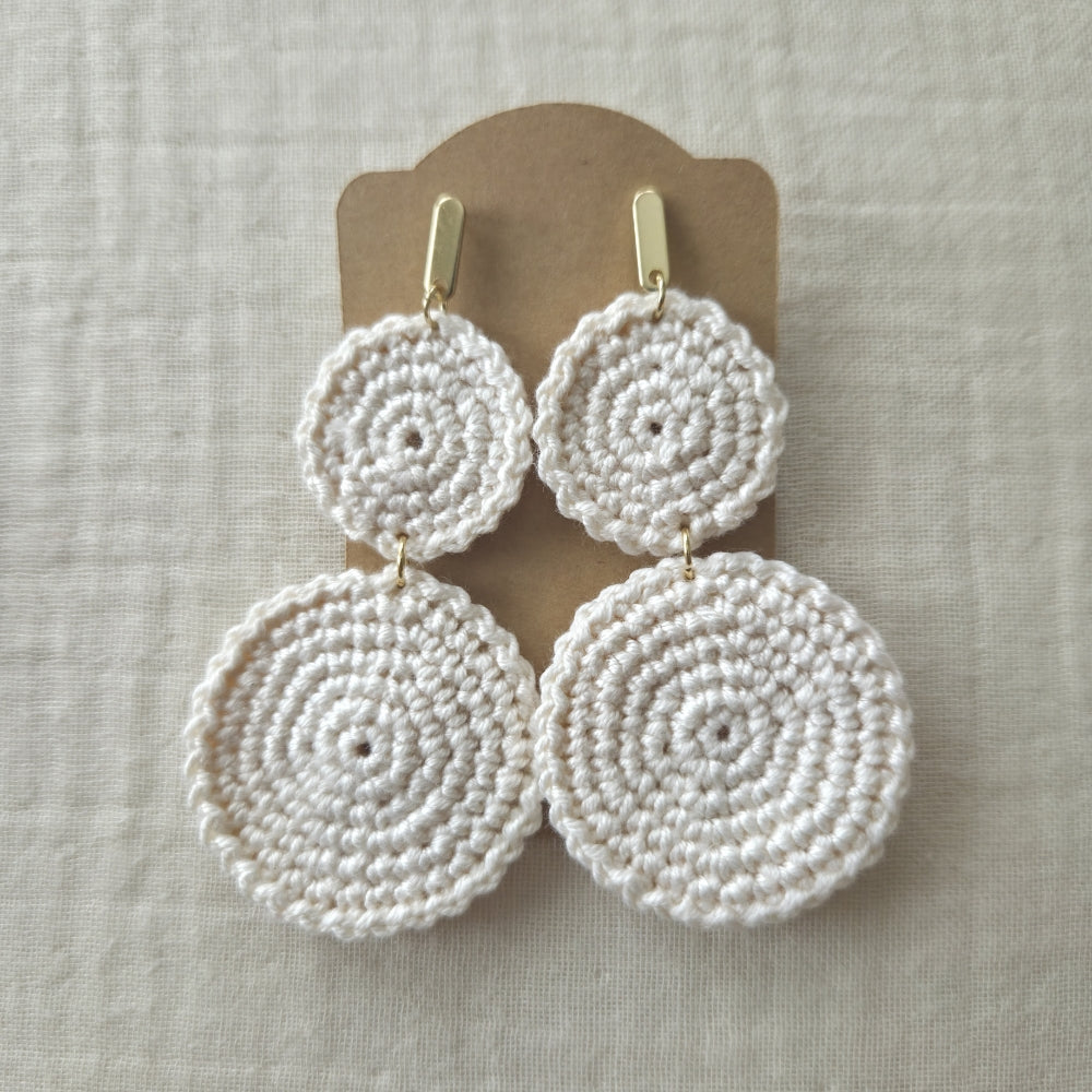 Set of white crocheted earrings on a beige card against a light background