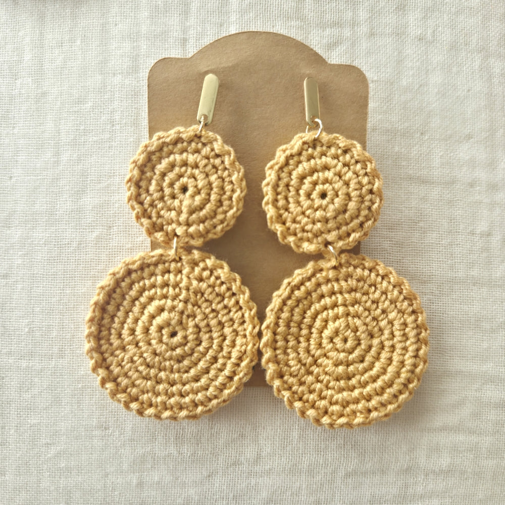 Pair of yellow crochet earrings on a wooden stand against a light background