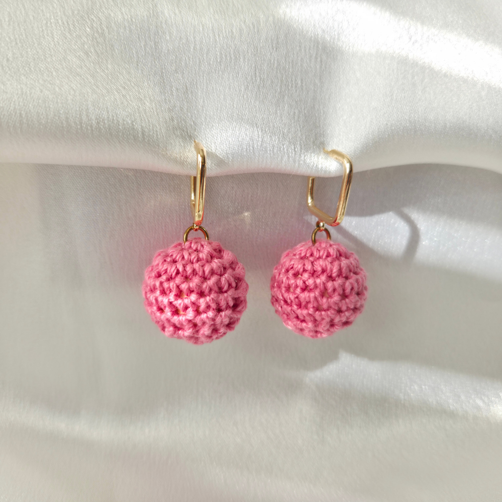 Pink crochet ball earrings on a white fabric background
