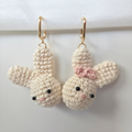 Pair of crocheted bunny earrings with a pink bow on a white background