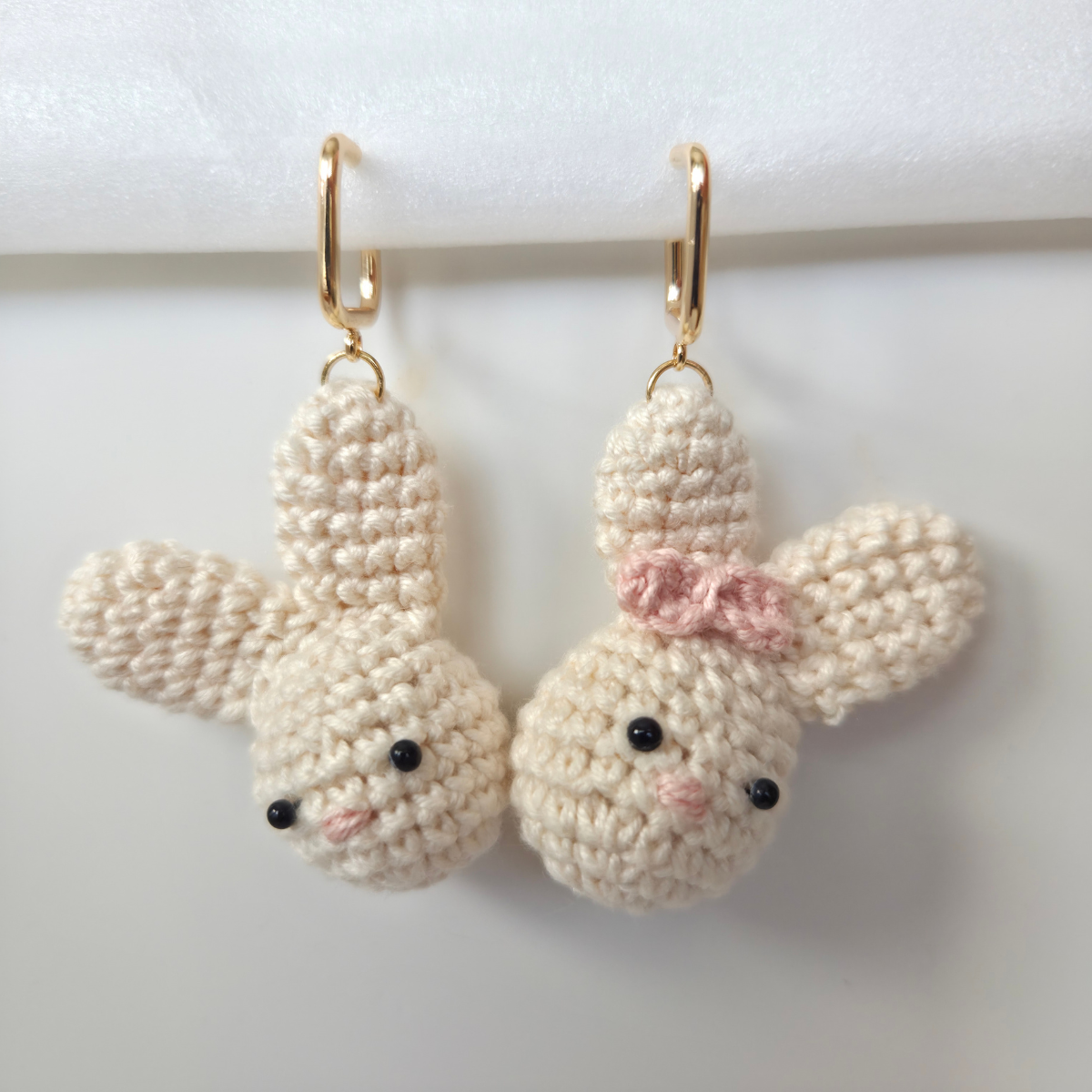 Pair of crocheted bunny earrings with a pink bow on a white background