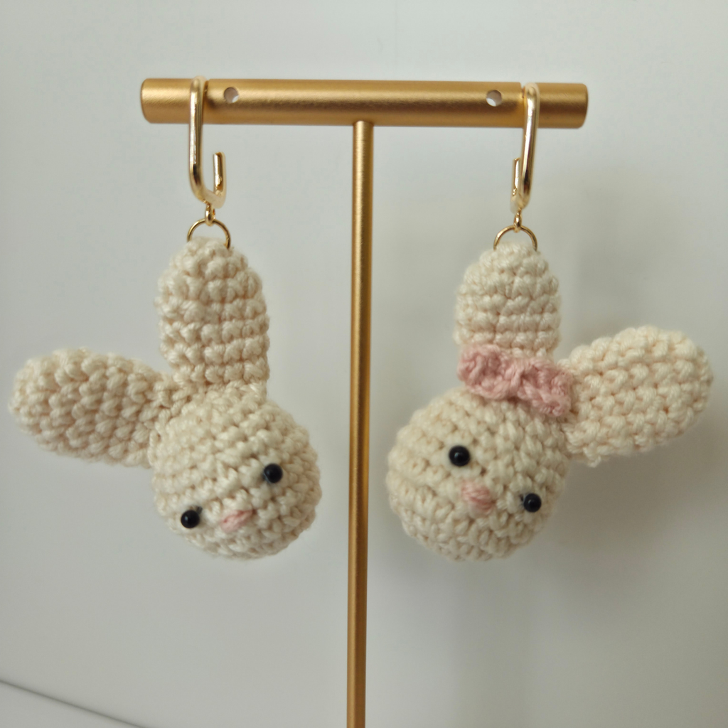 Pair of crochet bunny earrings on a gold stand against a light background