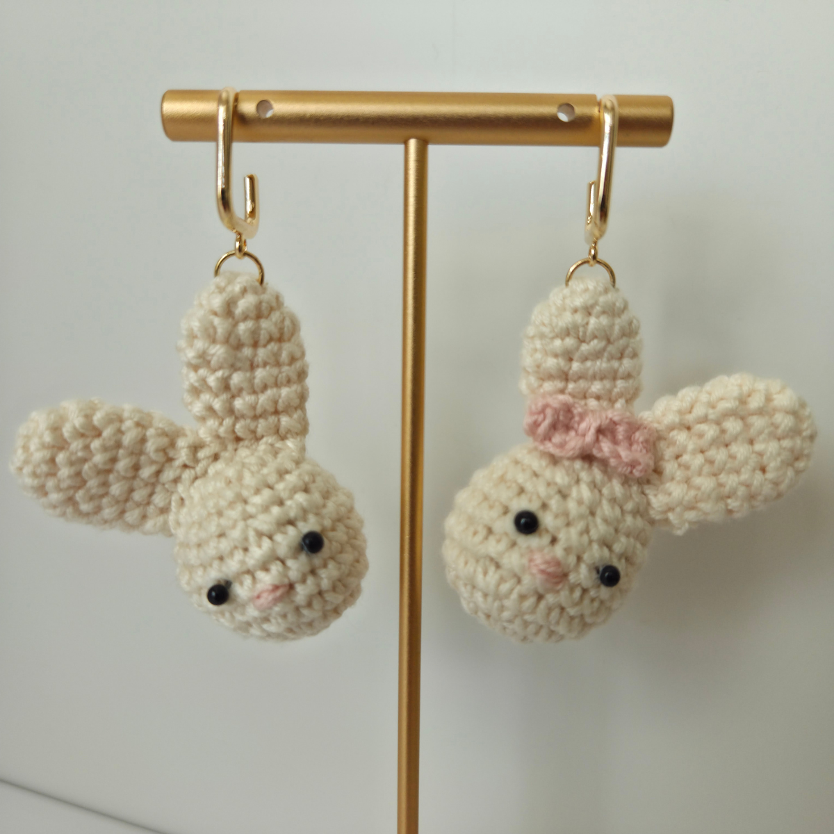 Pair of crochet bunny earrings on a gold stand against a light background