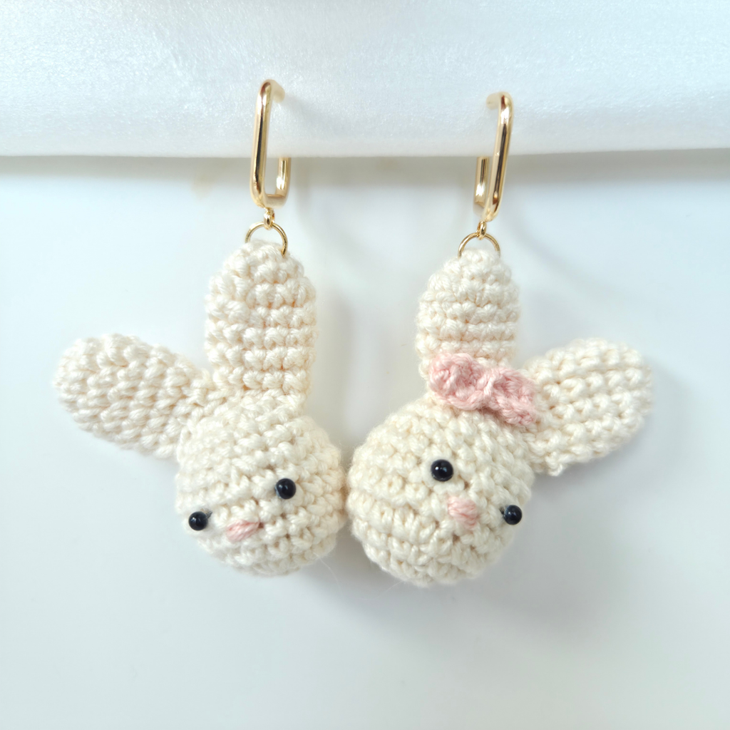 Pair of crocheted bunny earrings with a pink bow on a white background