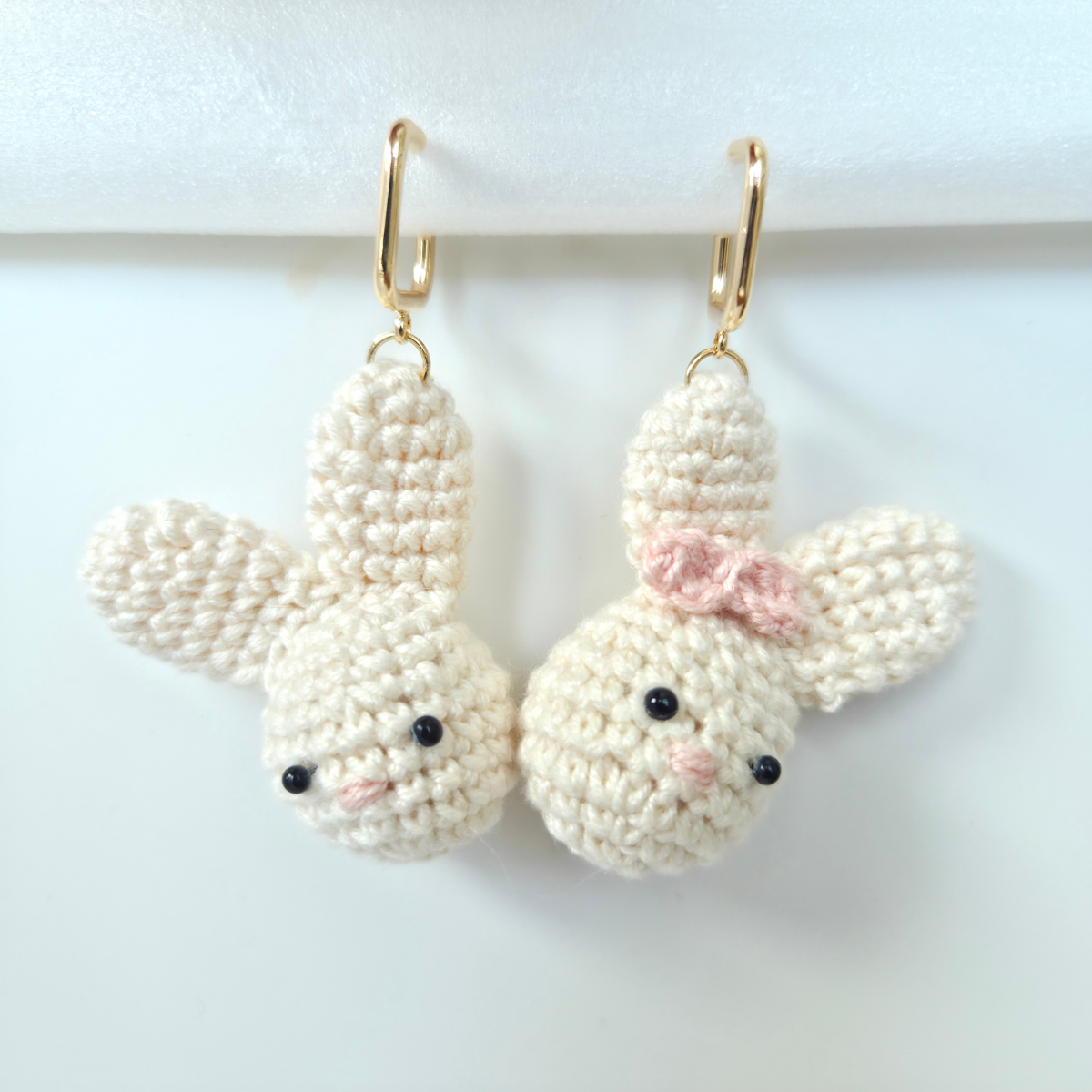 Pair of crocheted bunny earrings with a pink bow on a white background