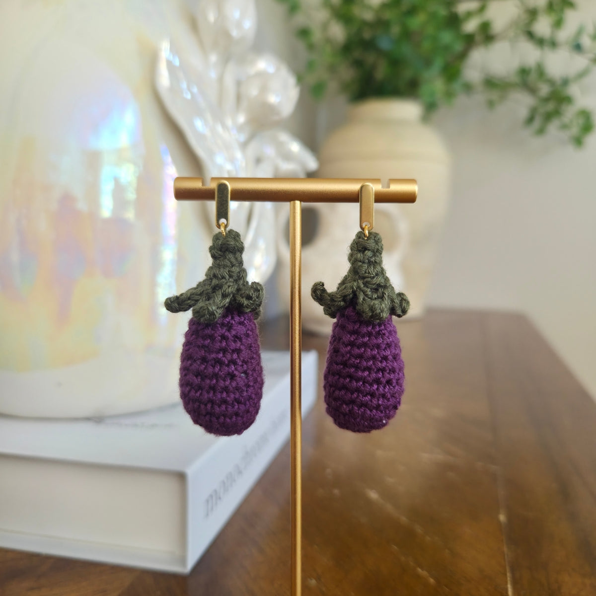 Purple and green crocheted earrings on a gold stand with a blurred background