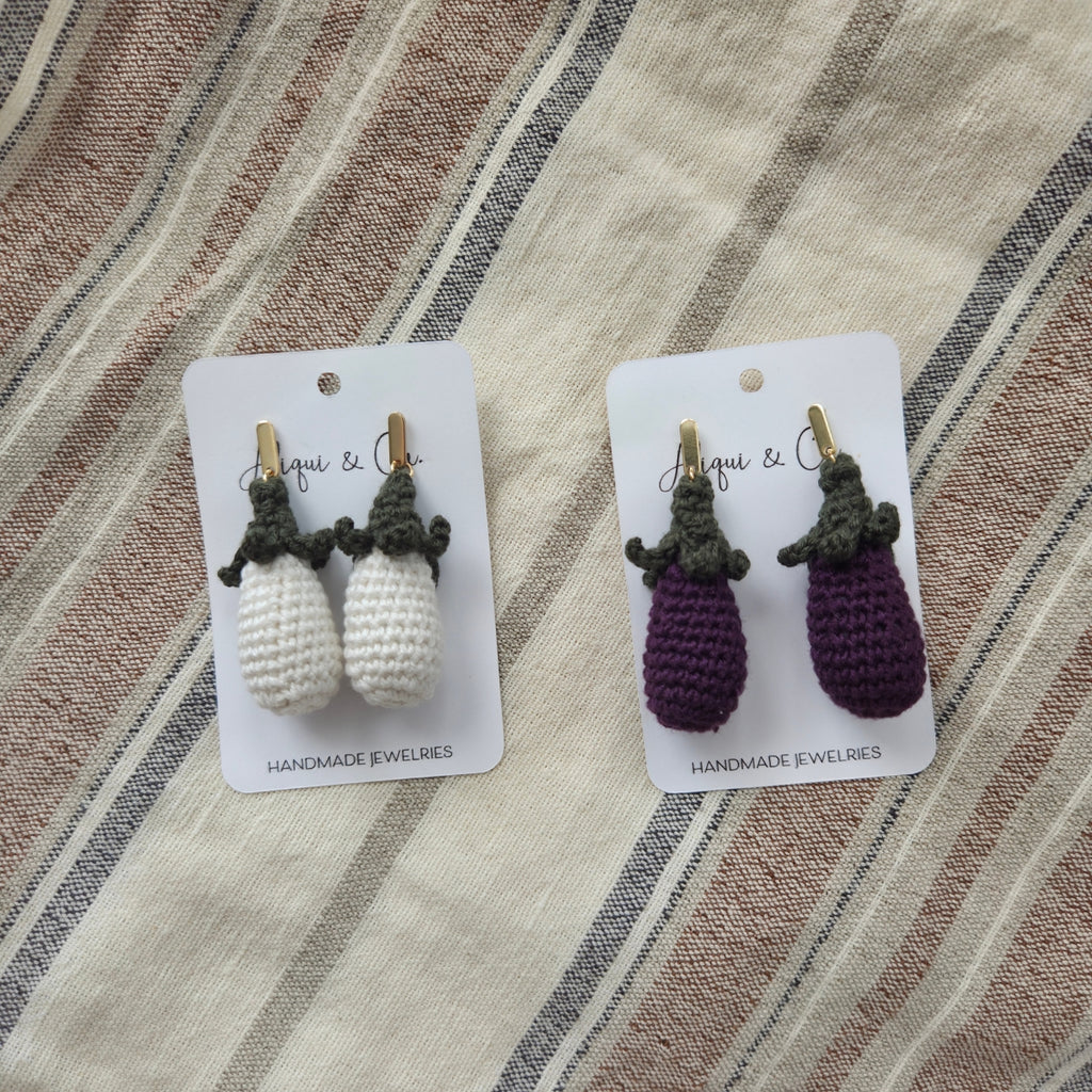 Pair of white and purple handmade crochet earrings on cards with a striped fabric background