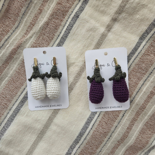Two pairs of handmade crochet eggplant earrings on cards with a striped fabric background