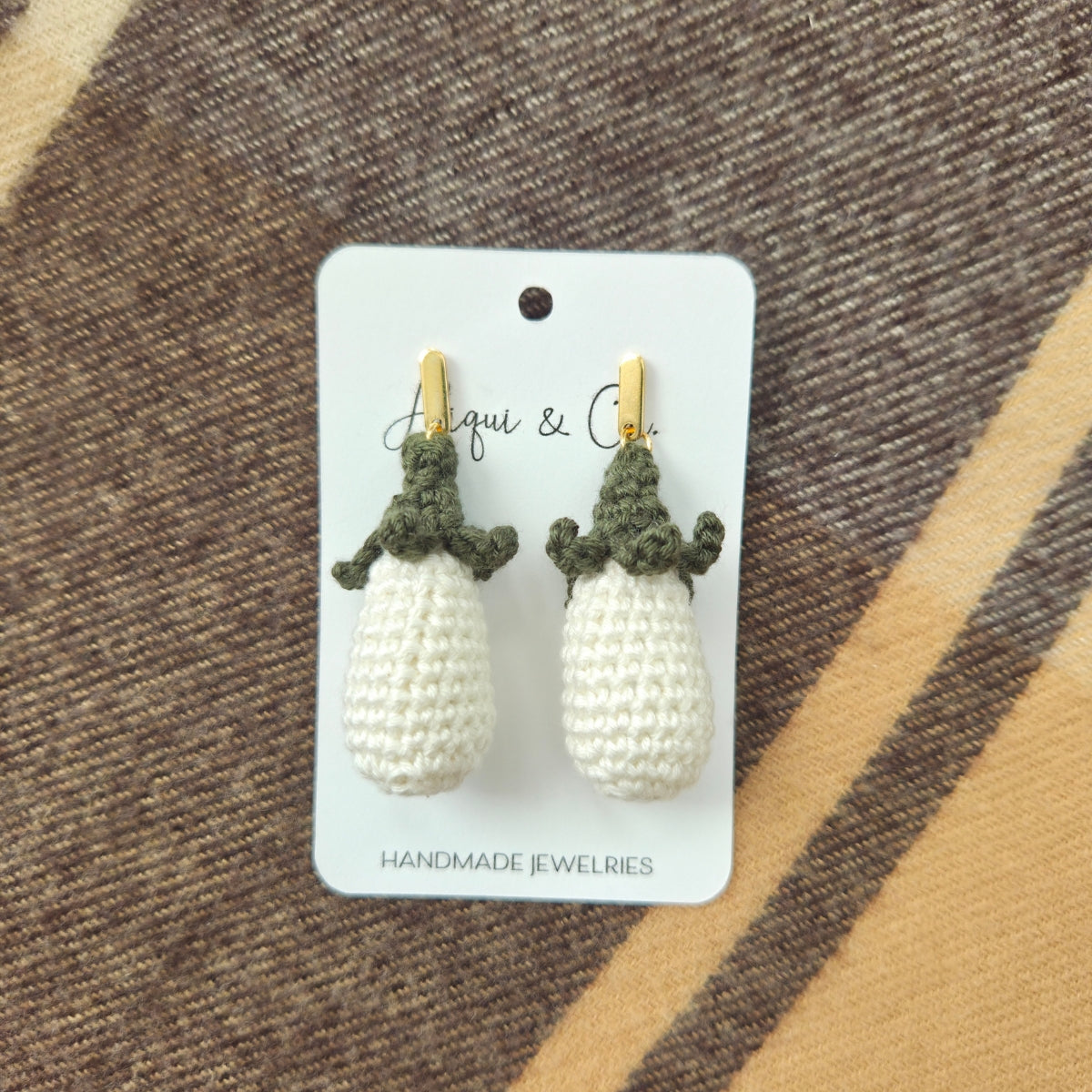 Crocheted white earrings on a card with a brown and beige striped background