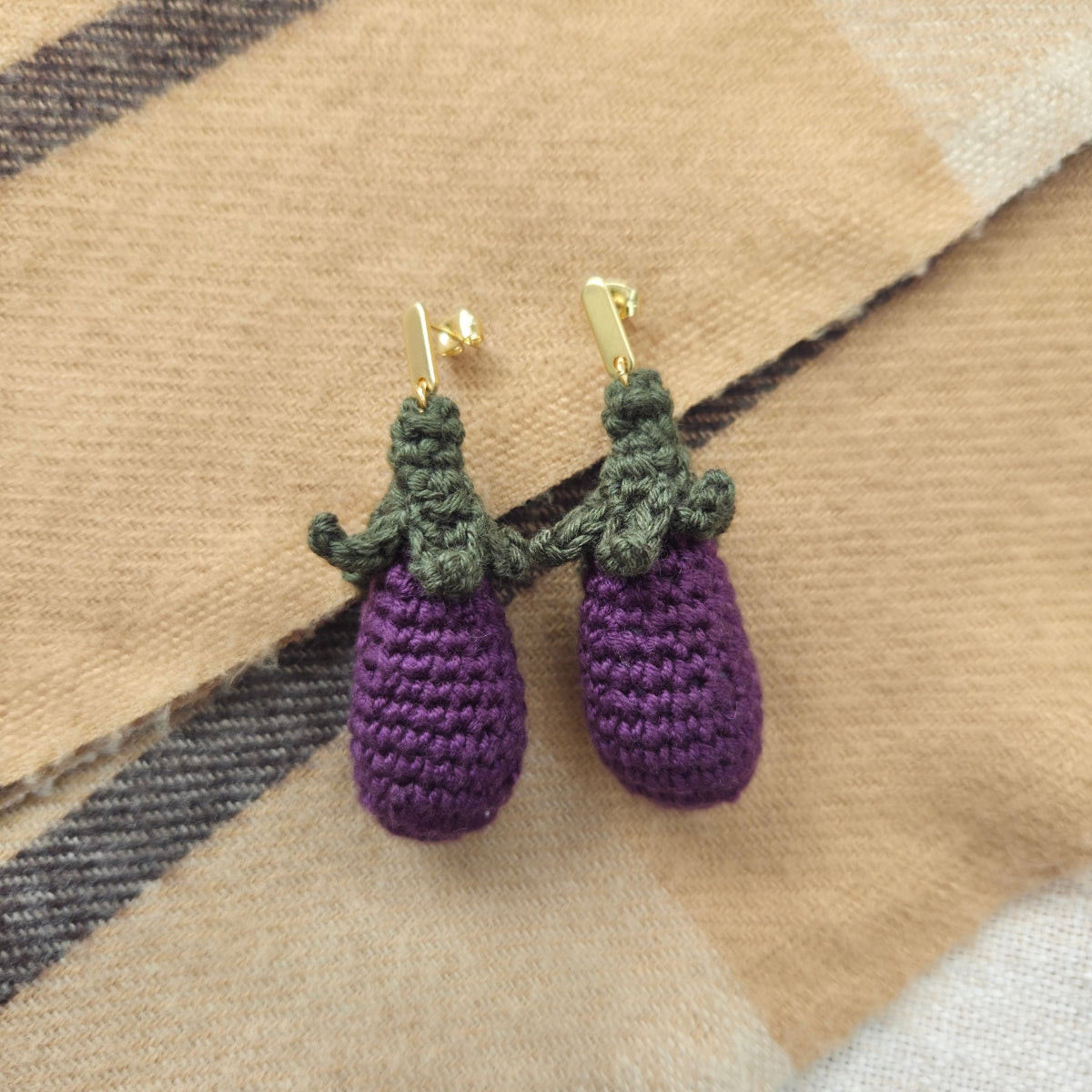 Crocheted eggplant earrings on a plaid fabric background