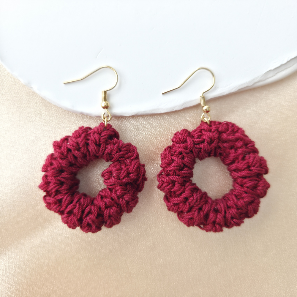 Red handmade earrings on a beige surface with a white plate in the background