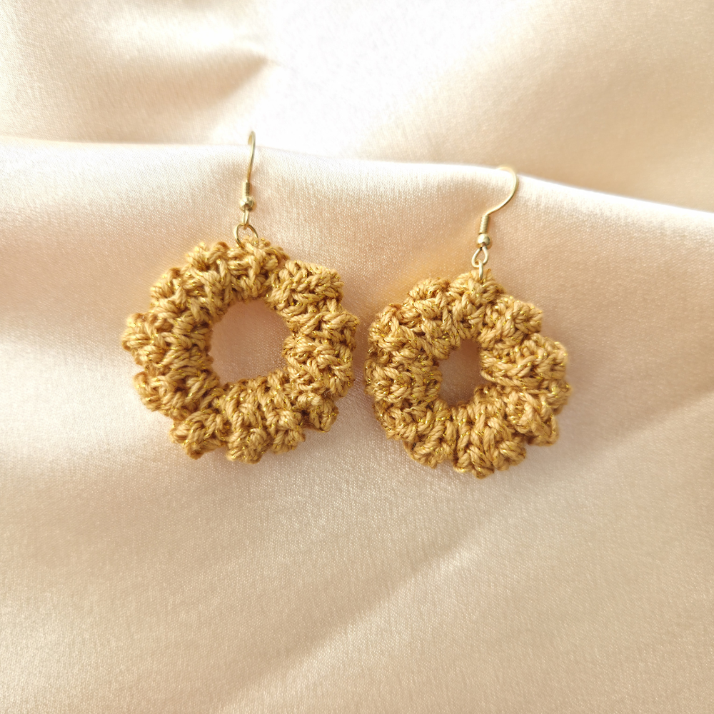 Pair of gold crochet earrings on a beige fabric background