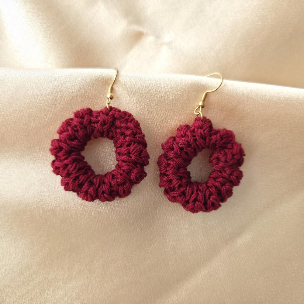 Pair of burgundy crochet twist hoop earrings on a beige fabric background
