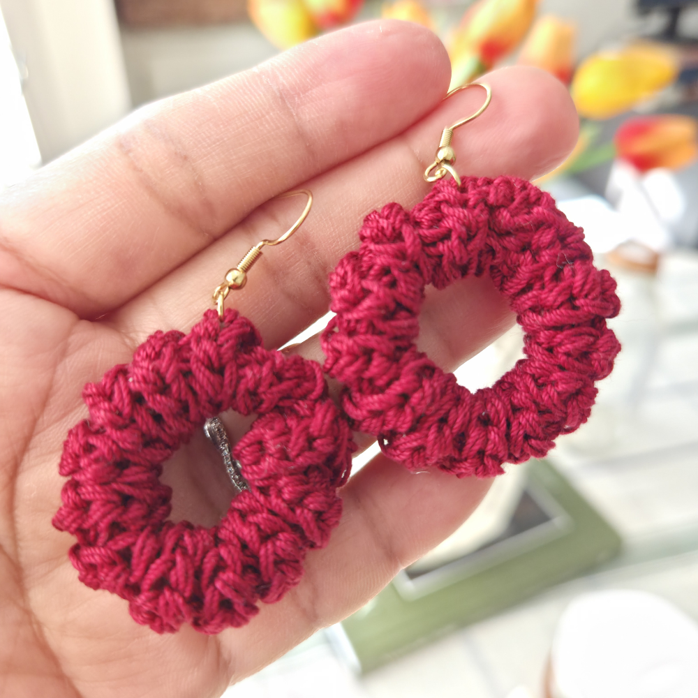 Red crochet earrings hoop held in a hand with a blurred background