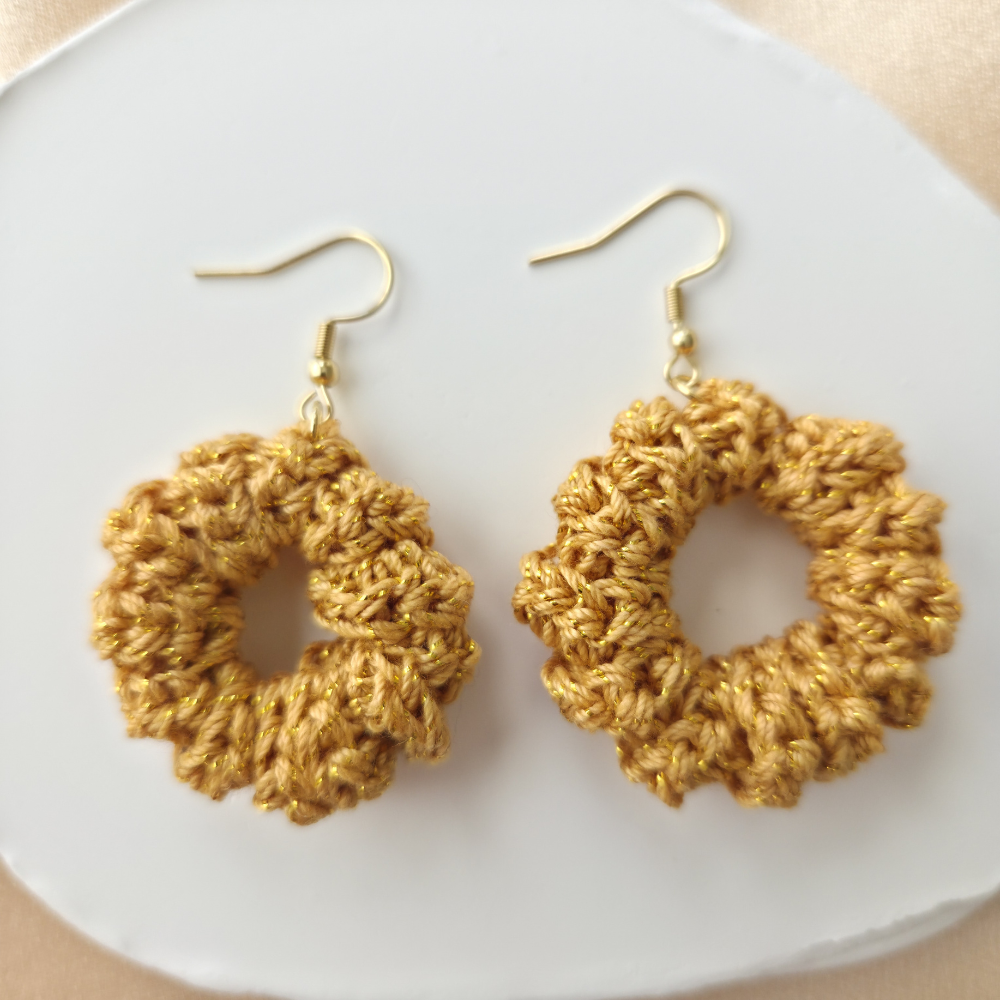 Pair of gold crochet earrings on a white plate.