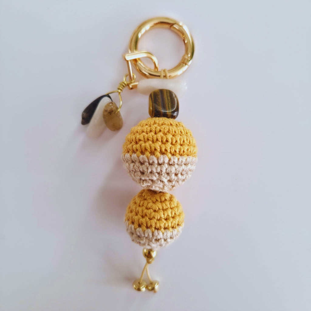 Crocheted keychain with gold accents on a light gray background