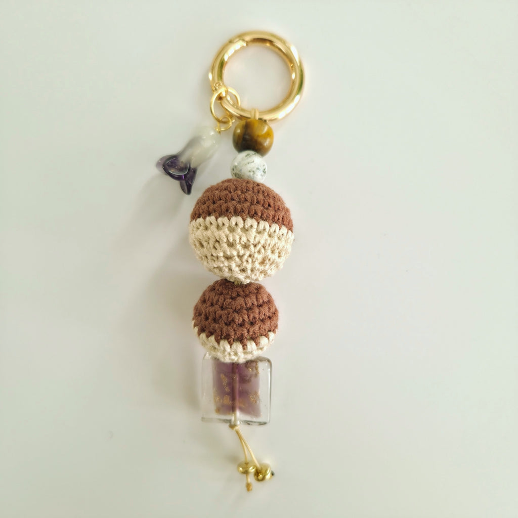 Crocheted keychain with beads and a small bottle charm on a light gray background