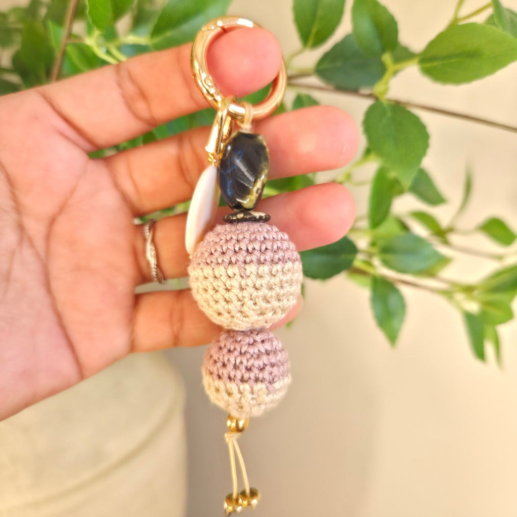 Hand holding a keychain with decorative beads against a blurred green background