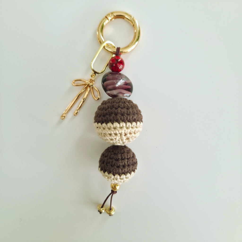 Keychain with brown and beige beads and a gold bow on a light gray background