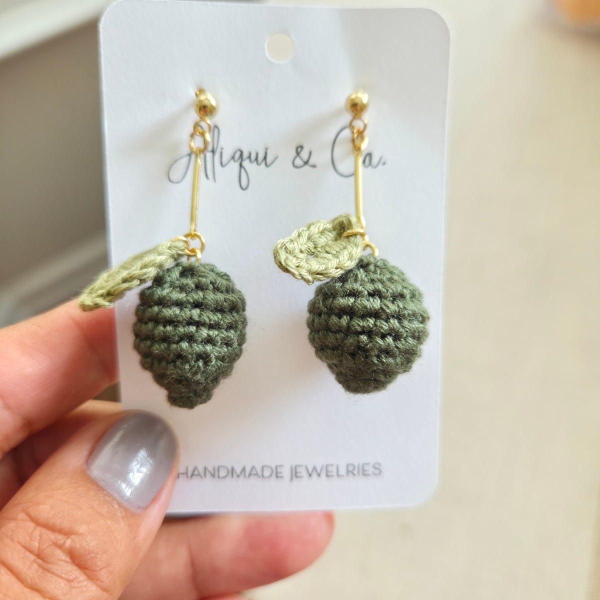 Green crochet lime earrings on a Aliqui & Co card held by a hand with gray nail polish.