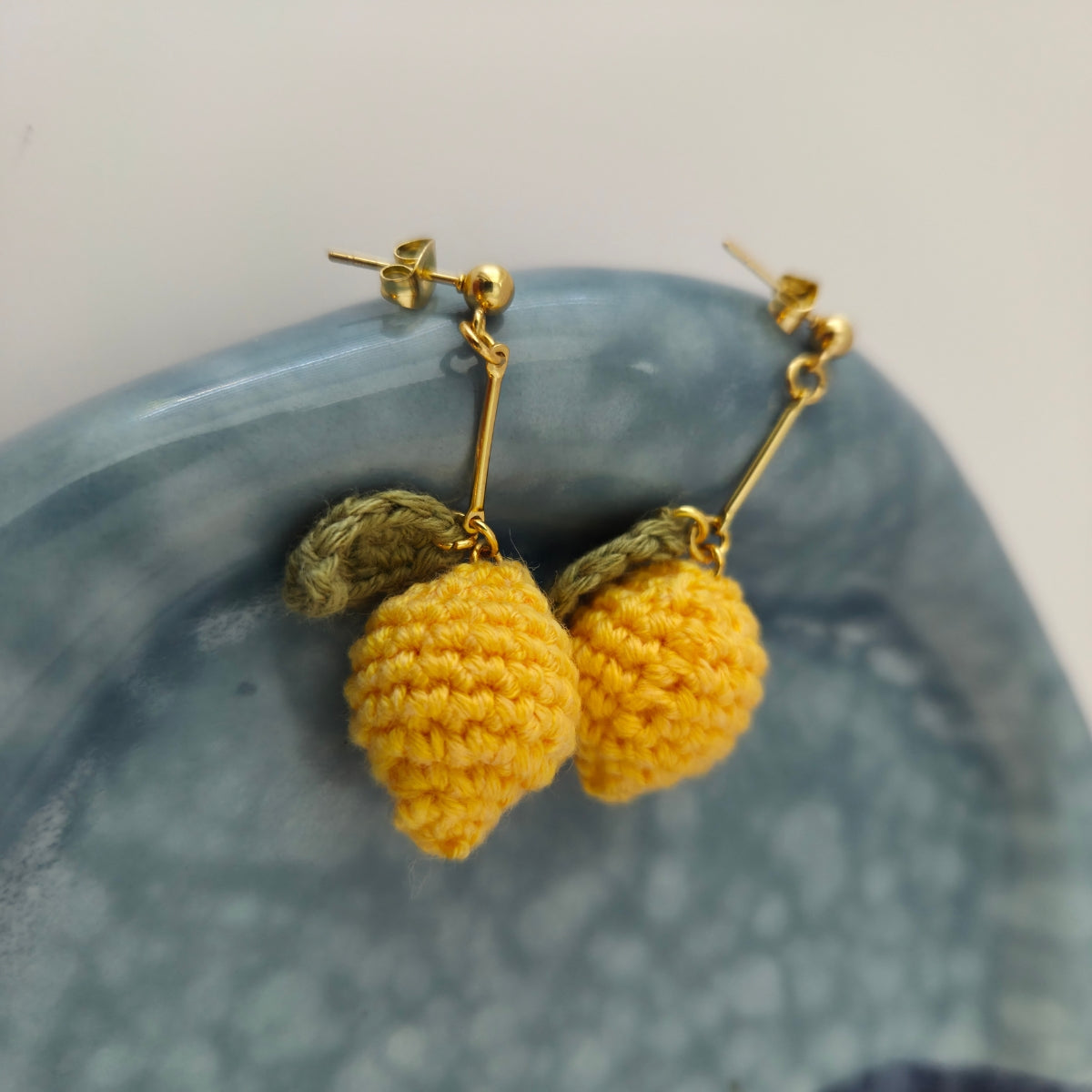 Yellow crochet earrings on a textured blue surface