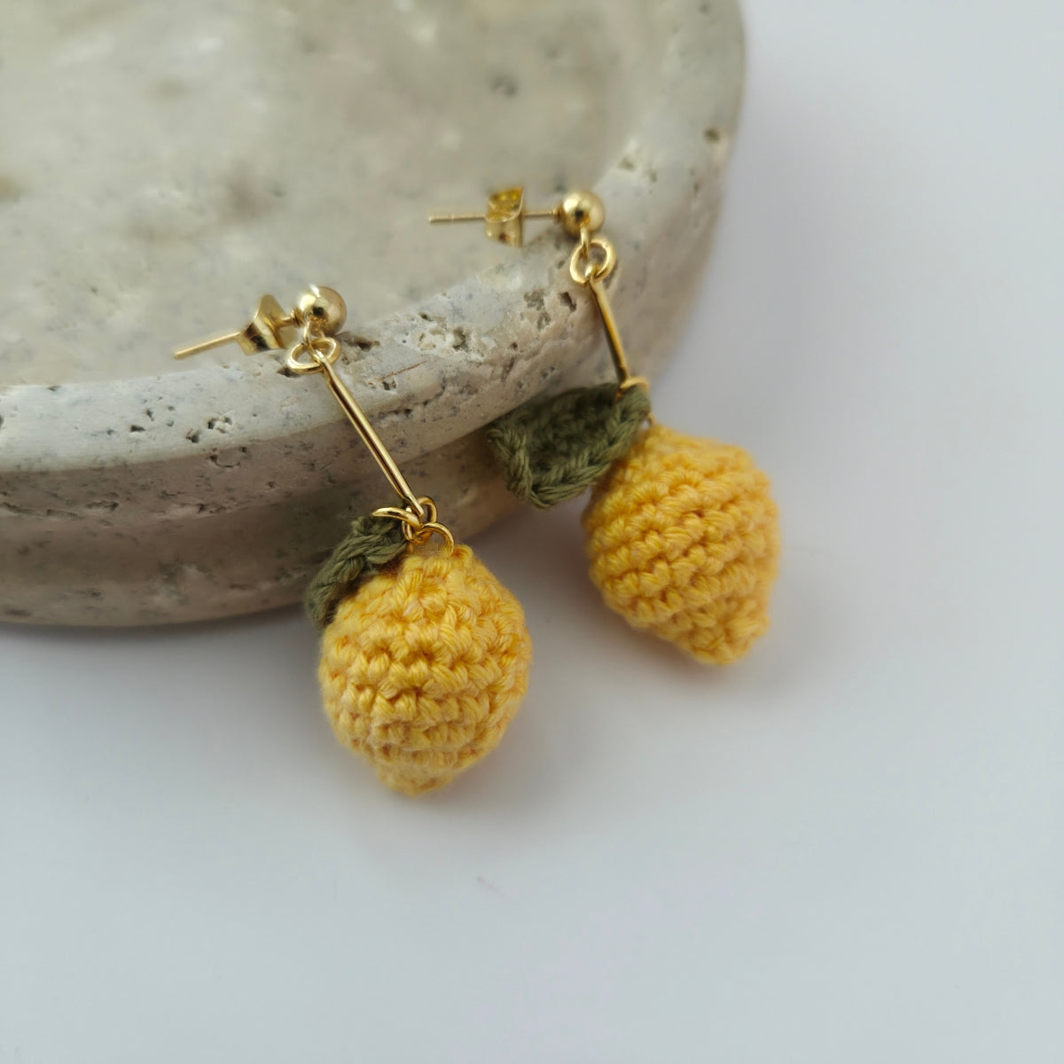 Pair of yellow lemon crochet earrings on a stone surface