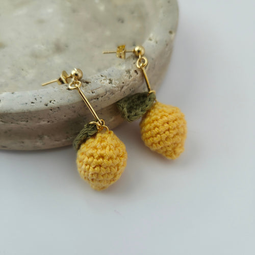 Pair of yellow lemon crochet earrings on a stone surface