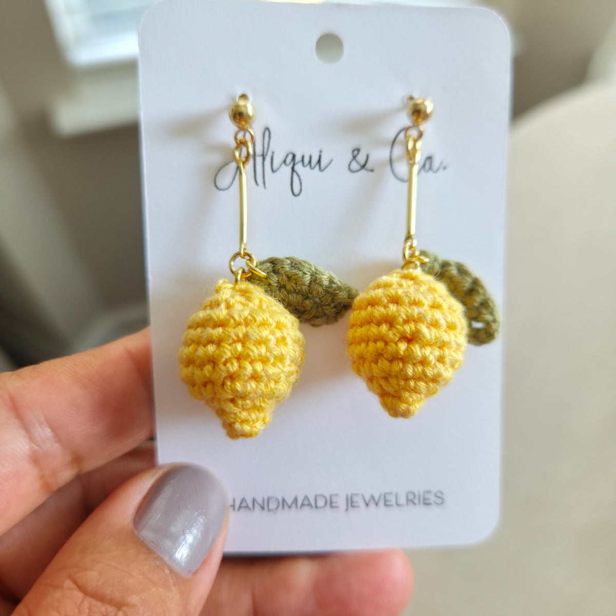 Handmade lemon-shaped earrings on a card held by a hand.